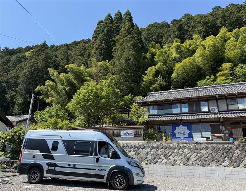 新緑の山を背にした古民家とキャンピングカー